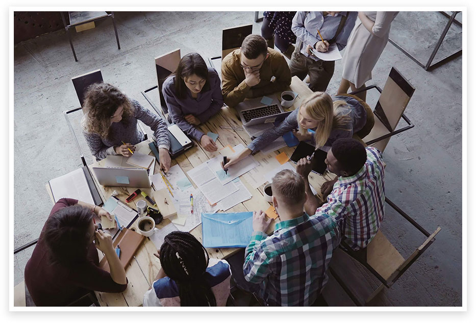 group of men and women crowded around a table and collaborating on a project